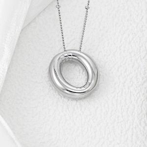 Macro shot of polished silver letter pendant on fine chain with silk accent background