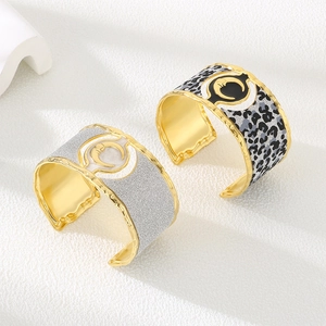 Detail of wide gold-plated cuff bracelets featuring sun and moon motifs in a textured finish