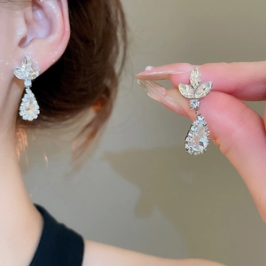 Detailed shot of silver wheat ear and pear-shaped rhinestone pendant earrings on model