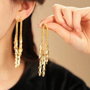Detailed view of long gold leaf tassel earrings worn by a model to show length