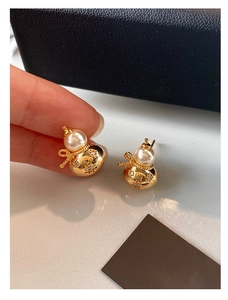 Détail de boucles d'oreilles gourde dorées avec perle blanche et nœud, travail délicat