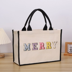 Detail of canvas tote bag with colorful MERRY lettering and black handles on wood table