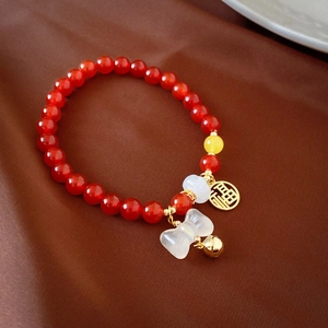 Détail macro du bracelet en cinabre rouge avec pendentif Fu doré, clochette et nœud