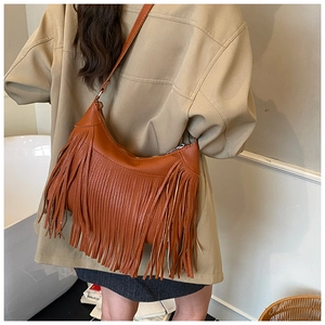 Close-up of brown leather tassel bucket bag worn by model showing bohemian fringe details