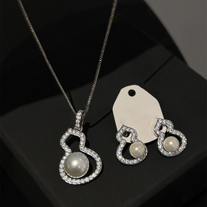 Elegant silver gourd jewelry set with sparkling crystals and white pearls on black surface