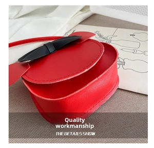 Detail showing red synthetic leather texture and black bow on a girl crossbody bag