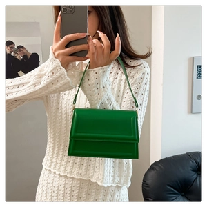 Detail of green minimalist crossbody bag with gold hardware held by a model in white