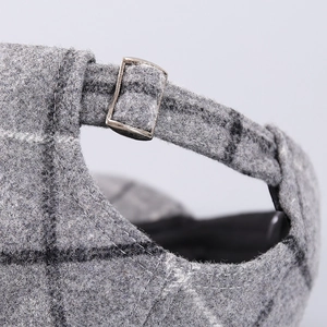 Detail of grey houndstooth wool cap with adjustable silver metal buckle and stitching