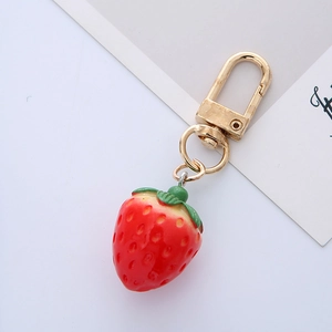 Macro view of a cute red strawberry keychain with detailed green leaves and gold clasp