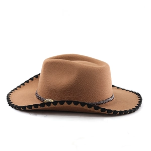 Detail of brown felt cowboy hat featuring woven band, metal ornament, and wavy black piping