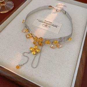 Macro detail of vintage silver woven necklace with yellow crystal flowers on a display tray