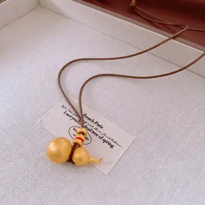 Oriental style necklace featuring a matte gold gourd pendant on a brown braided leather cord