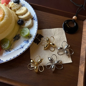 Macro detail of tulip flower stud earrings in gold and silver finish on a beige napkin