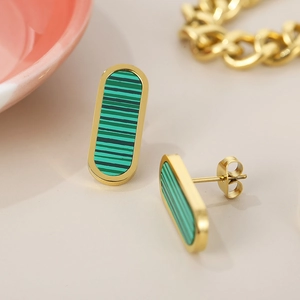 Close-up of gold-plated stud earrings with green striped inlay on a beige table