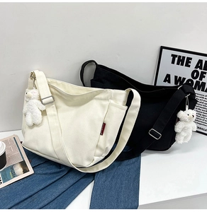 Large canvas crossbody bags in black and white with cute teddy bear pendants set on a table