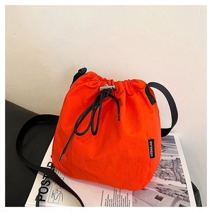 Detail of bright orange drawstring bucket bag with black strap on a studio magazine