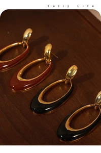 Detail of oval enamel drop earrings in burgundy and black with gold metal borders