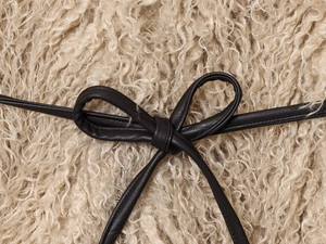 Detail of black leather bow tie accessory on soft beige curly faux fur texture fabric