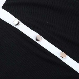 Dettaglio macro in maglia a costine nera con bordo bianco e tre bottoni in metallo oro