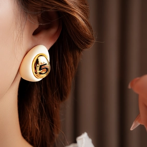 Close-up of model wearing gold-plated teardrop earrings with beige resin and number 5
