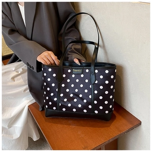 Minimalist black tote bag with white polka dots and gold logo patch on a wood bench