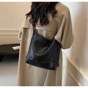 Close-up of black tote bag with woven texture on model in beige trench coat