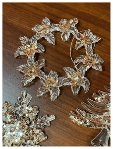 Detailed flat lay of acrylic Christmas snowflake ornaments with gold sequins on wood