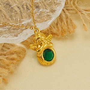 Gros plan d'un pendentif ange plaqué or 18k avec une pierre verte sur tissu texturé