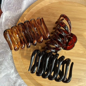 Three glossy pumpkin-shaped hair claws in amber, brown, and black on a wooden tray