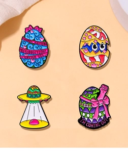 Detail of four colorful Easter enamel pins featuring egg shells and dinosaur designs