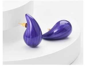 Macro detail of teardrop earring featuring dark purple brushed texture and golden studs