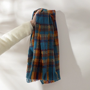 Detail of soft knitted scarf featuring orange and blue plaid pattern with fringe edges
