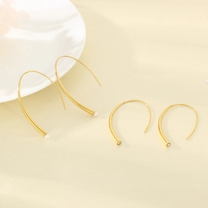 Detail of gold minimalist ear hooks featuring white pearls and zircon accents on beige background