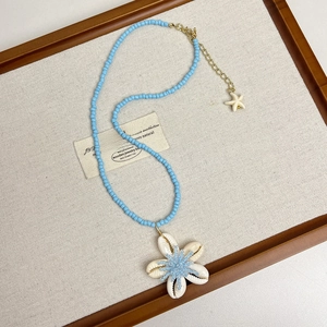 Dettaglio di collana boho con perline blu, fiore di conchiglia bianca e ciondolo stella