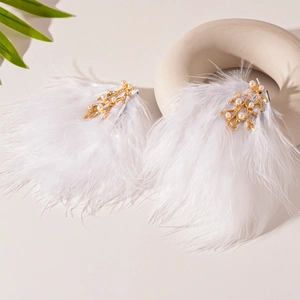 Détail de boucles d'oreilles en plumes blanches avec branches dorées et perles sur céramique