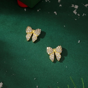 Detail of golden bow-shaped stud earrings featuring shimmering zircon pavé on a festive base