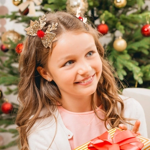 Glittery gold reindeer antler hair clips with red pom-poms worn by a child for Christmas