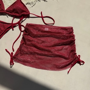 Bikini rouge scintillant avec paréo en résille assorti posé sur un fond de sable clair