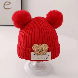 Detail of red knit infant hat featuring soft twin pom-poms and cute bear patch design