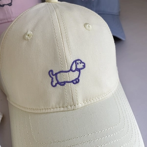 Creamy beige cotton baseball cap featuring purple dachshund embroidery with a curved brim
