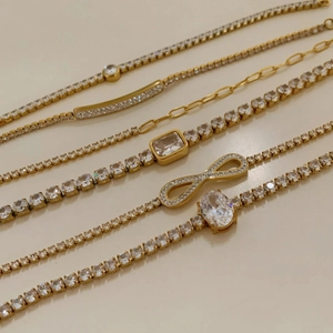 Detail of gold chain bracelets with zircon stones and infinity charms on white background