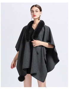 Detail of grey knitted poncho with thick black faux fur collar and decorative pom-poms