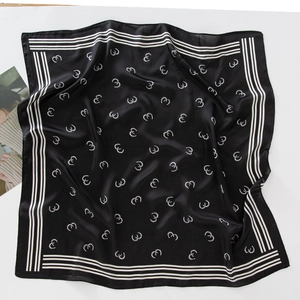 Detailed top view of black silk scarf featuring white horseshoe patterns and border stripes