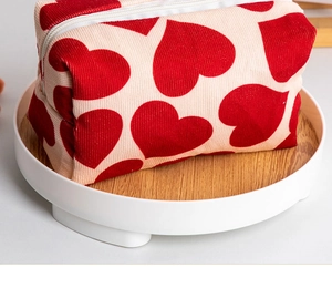 Detail of red heart patterns on cream corduroy makeup bag with white zipper closure