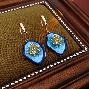 Close-up of vintage flower earrings with blue enamel petals and gold hooks on velvet