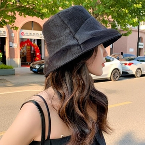 Women's black pleated bucket hat with bow detail shown in outdoor natural light setting