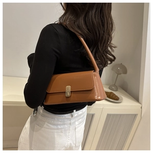 Detail of a brown leather shoulder bag with metallic clasp worn by a fashion model