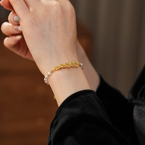 Detail view of pearl beaded bracelet with a gold-tone hollow metal charm on a woman's wrist