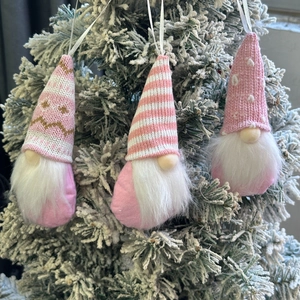 Three pink Christmas gnomes with knitted hats hanging on a snowy tree branch