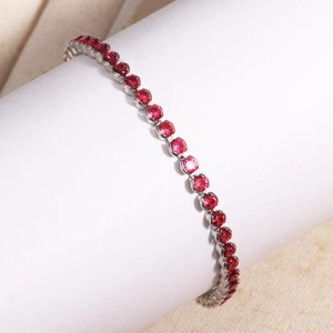 Macro shot of silver tennis bracelet featuring round red crystals on a white pedestal
